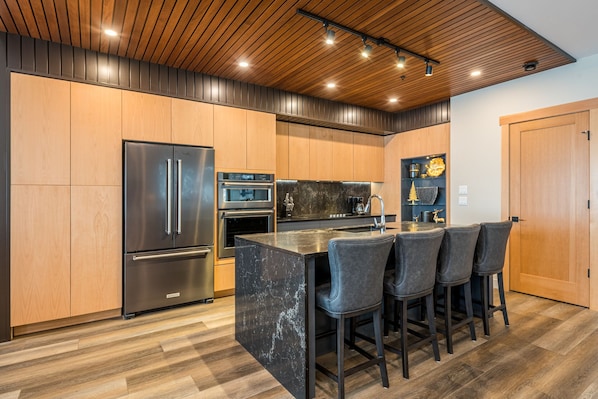 A modern kitchen with wooden cabinets, stainless steel appliances, a marble island, and bar stools.