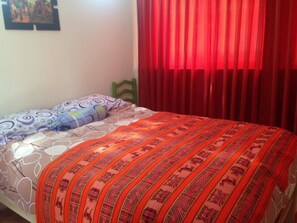 A bed with patterned bedding, a pillow, and a red curtain. - Casa de Ana Huaraz (Independencia)