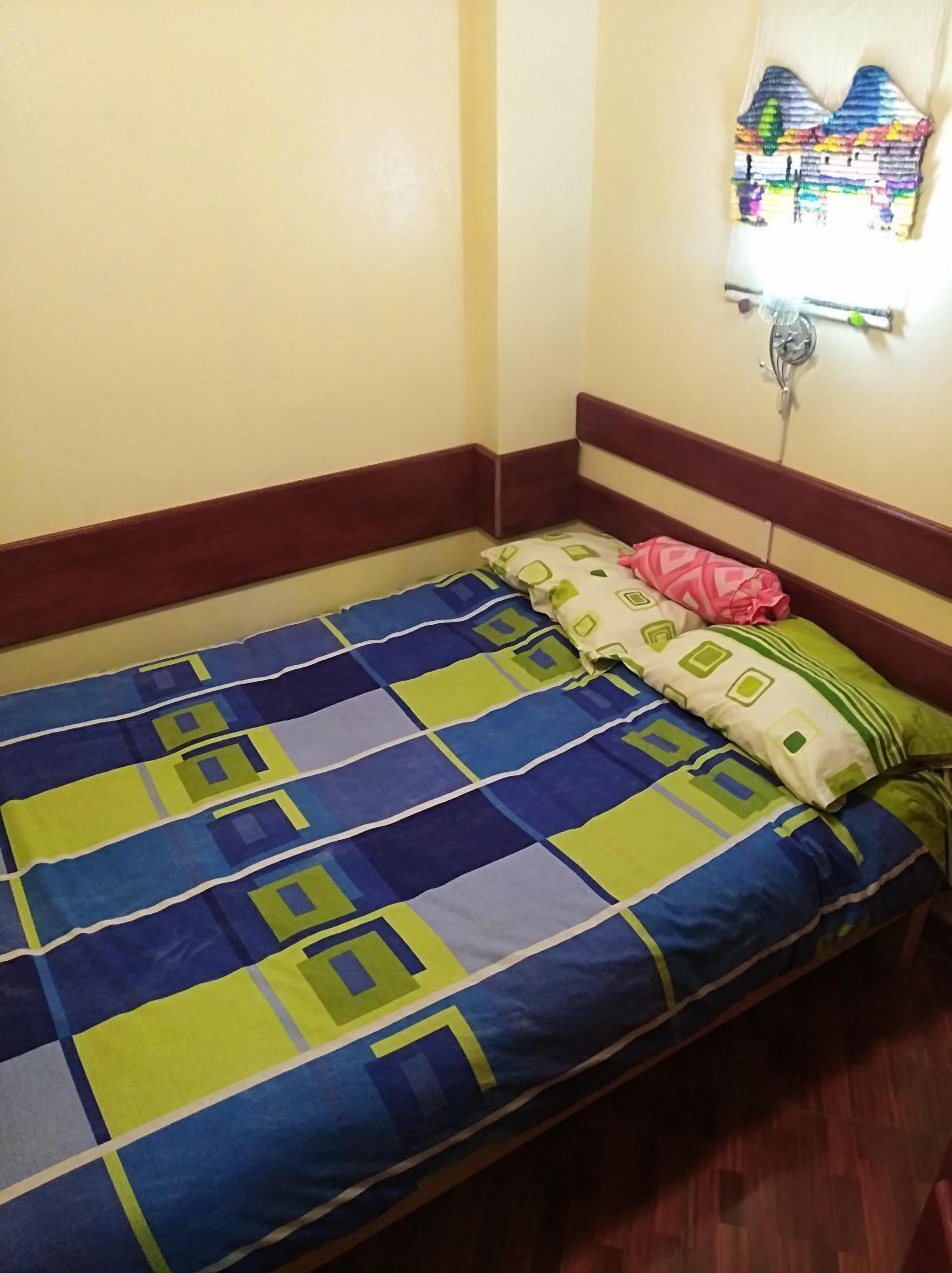 A single bed with a blue and green checkered bedspread and multiple pillows, including a pink one.