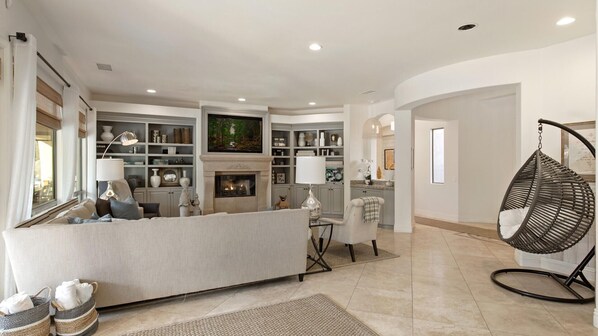 A spacious living room with a fireplace, a sofa, a hanging chair, and a well-organized bookshelf.