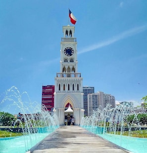A clock tower with a flag, surrounded by a water fountain display. - Apartment Alma Capital ocean view (Iquique)