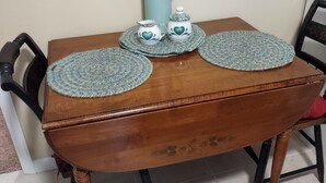 Een houten tafel met twee gevlochten placemats, een karaf en twee kleine decoratieve potjes.
