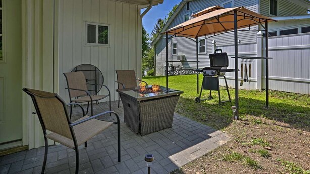 Een terras buiten met een tafel, stoelen, een vuurkuil en een barbecue.