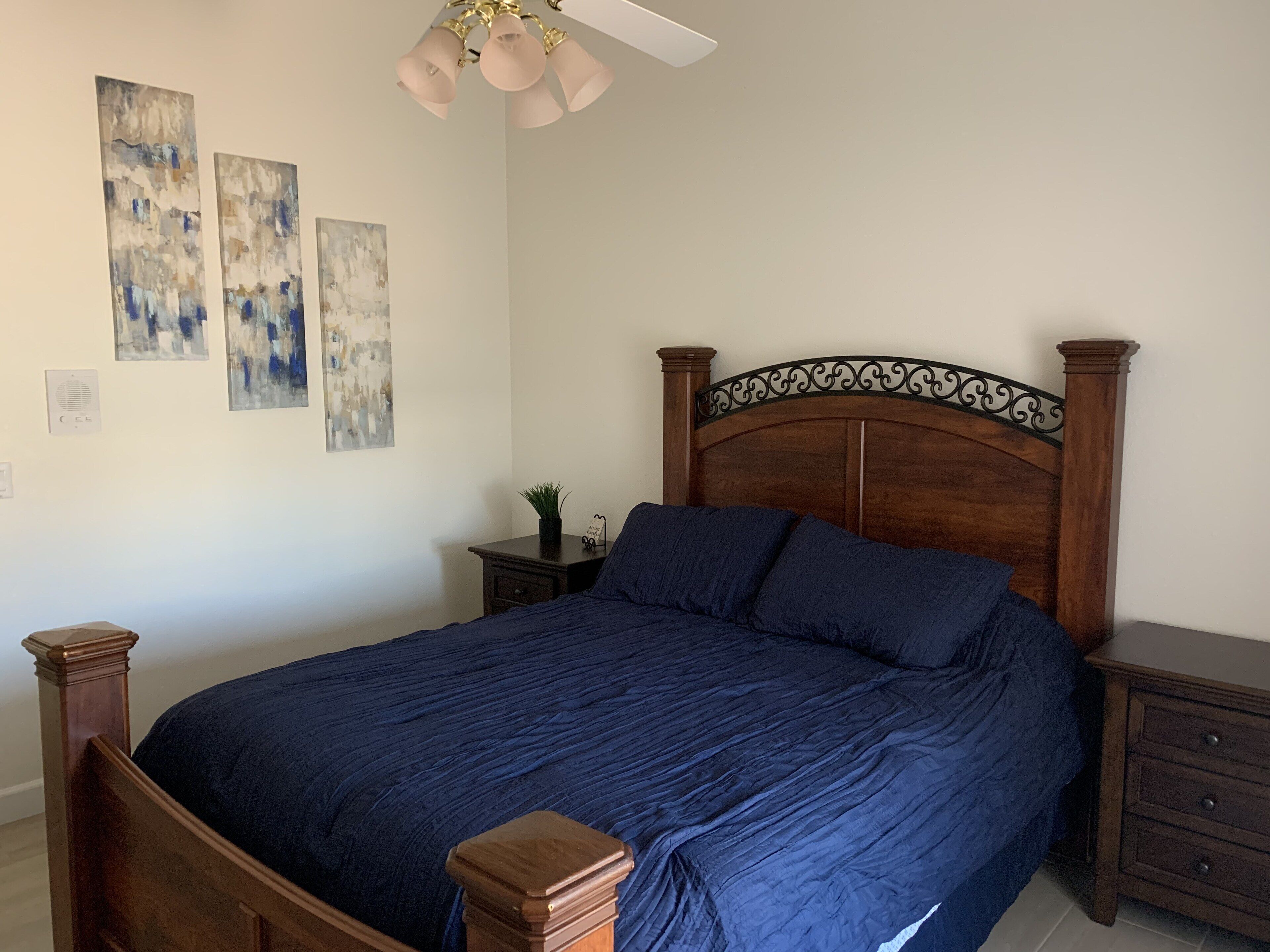 A bedroom with a large bed, a nightstand, a wall-mounted ceiling fan, and abstract art on the wall.