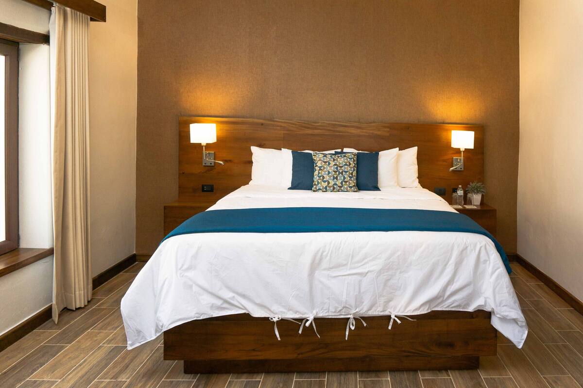 Ein Hotelzimmer mit einem großen Bett, einem Holz-Kopfteil, zwei Nachttischlampen und einem Fenster mit Vorhängen.