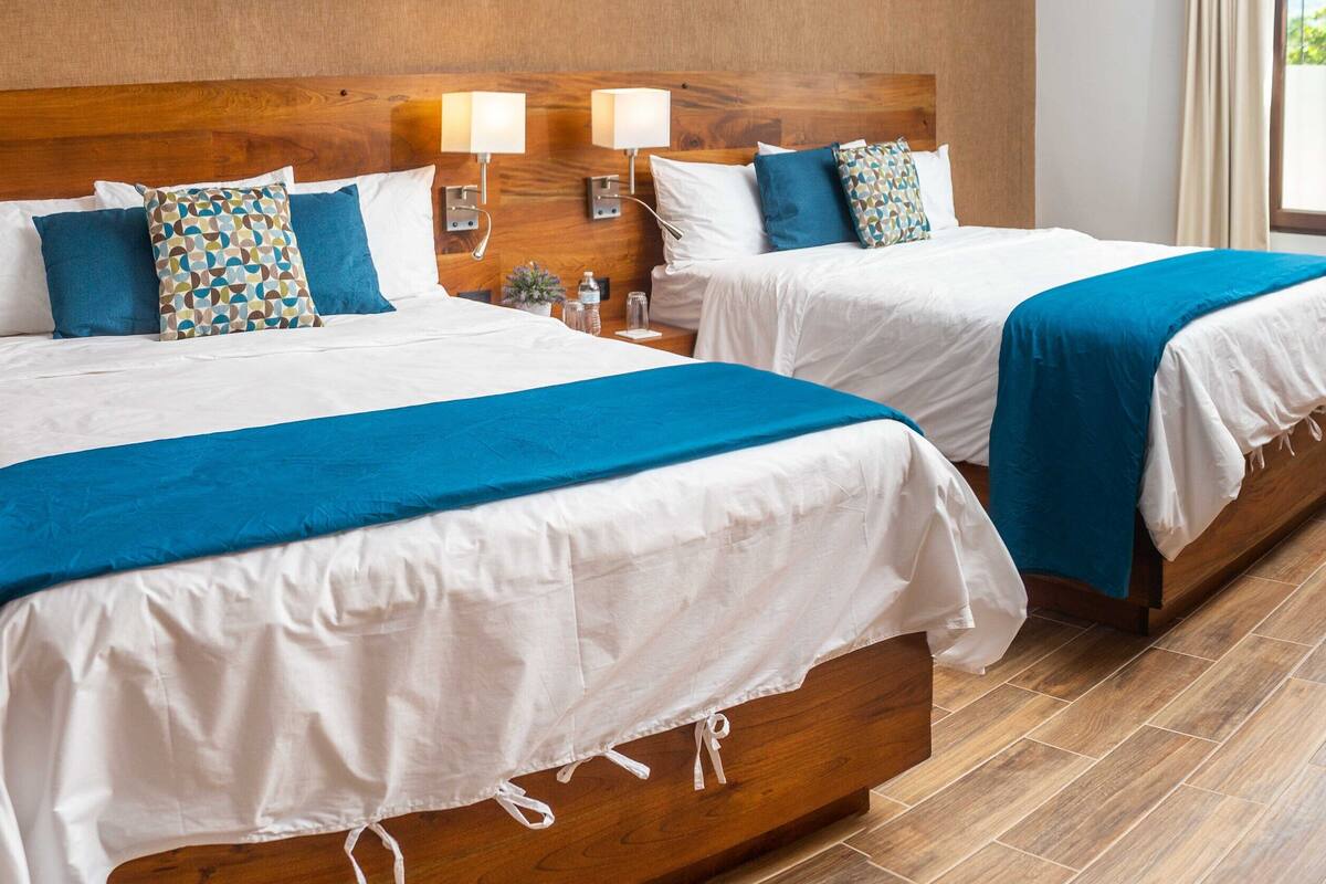 Zwei Doppelbetten mit weißer und blauer Bettwäsche, Holz-Kopfteile, Nachttischlampen und ein Holzboden.