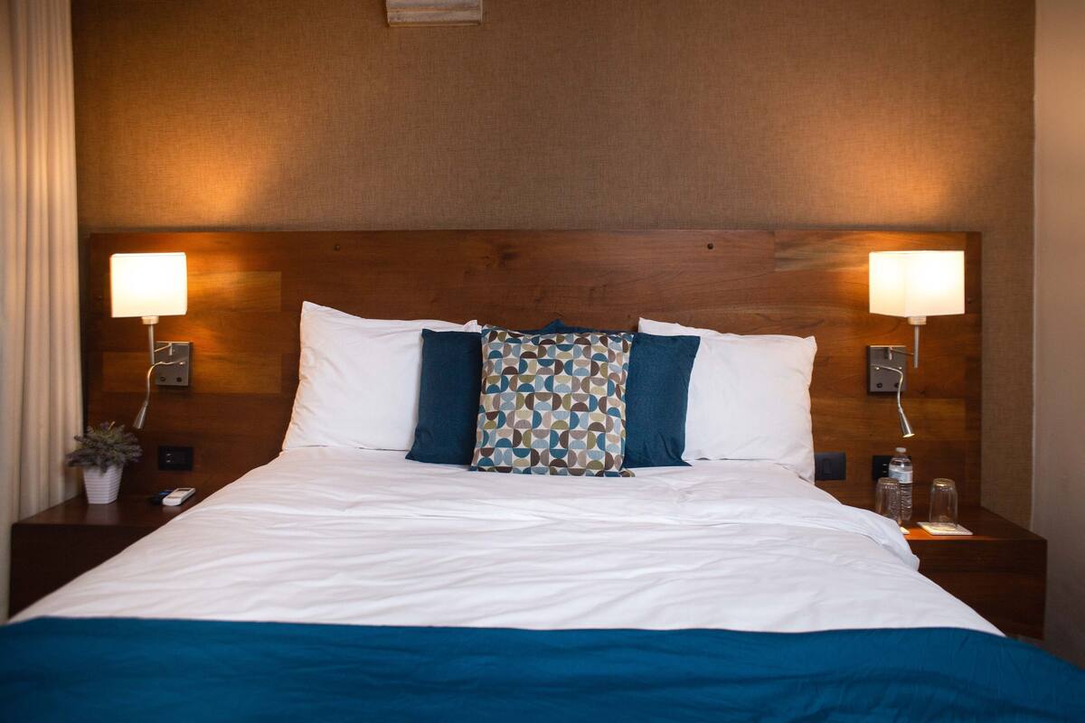 Ein ordentlich gemachtes Bett mit weißer und blauer Bettwäsche, zwei Nachttischlampen und einem hölzernen Kopfteil.
