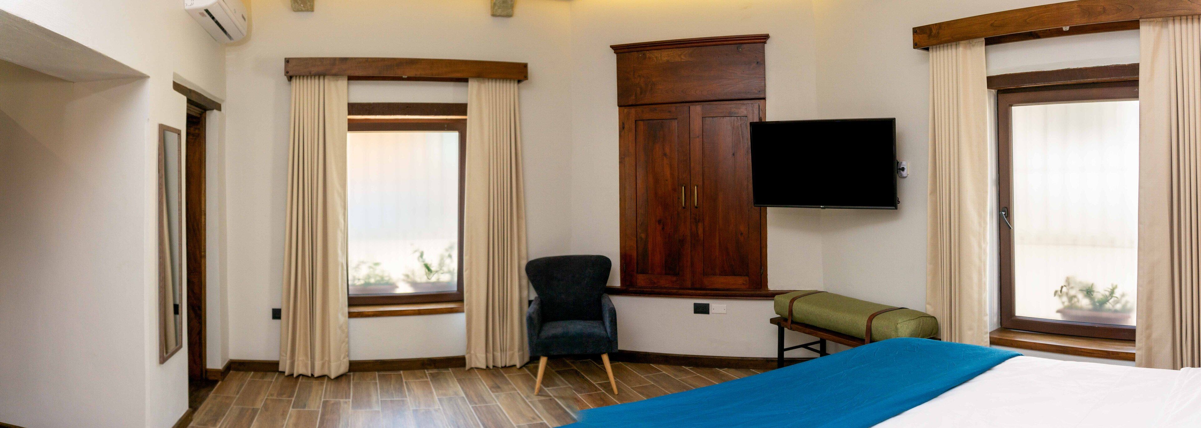 A hotel room with a bed, a TV, a chair, a wooden cabinet, and a window with curtains.