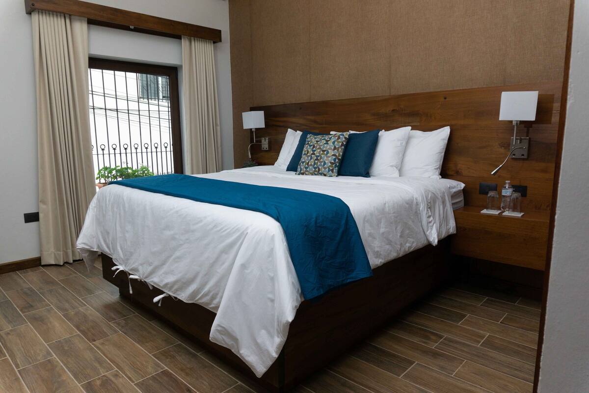 Ein großes Bett mit Holz Kopfteil, weißer und blauer Bettwäsche und zwei Nachttischlampen.