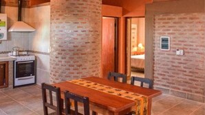 A kitchen with a brick wall, a wooden table, and chairs. - Cabañas Villa del Sol (Rosario de Lerma)