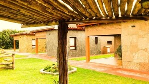 A courtyard with stone buildings, a wooden pergola, and a well-maintained lawn. - Cabañas Villa del Sol (Rosario de Lerma)