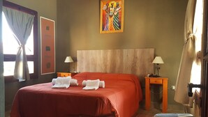 A hotel room with a large bed, two bedside tables with lamps, a painting on the wall, and a window with curtains. - Cabañas Villa del Sol (Rosario de Lerma)