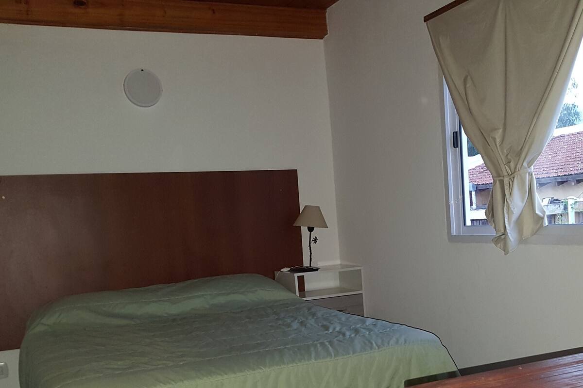 Un dormitorio con cama, mesita de noche, lámpara y ventana con cortinas.
