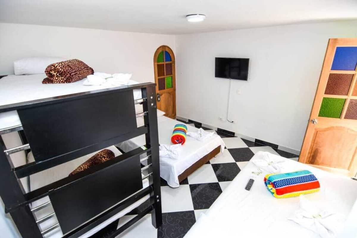 A room with bunk beds, a television, a wooden door with a colorful window, and a checkered floor.