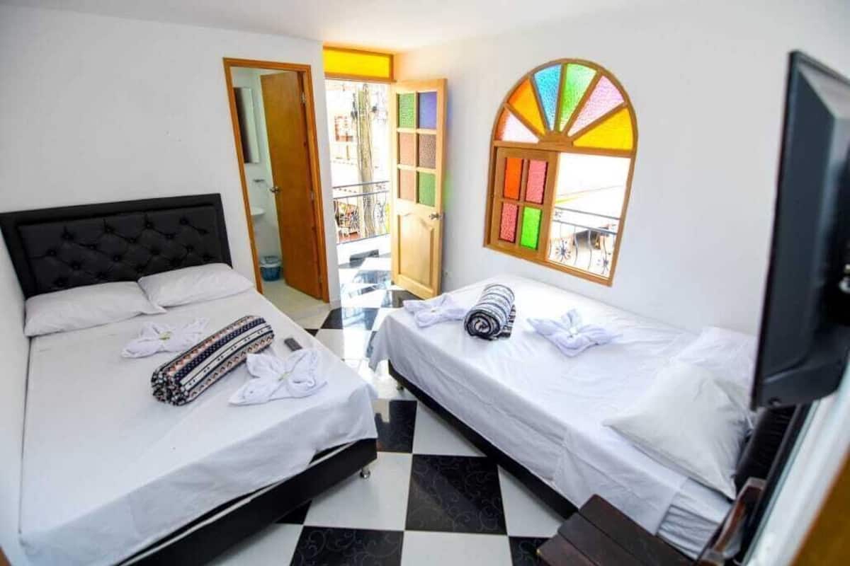A hotel room with two beds, a television, a window with a colorful stained glass design, and a checkered floor.
