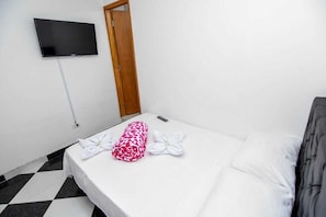 A hotel room with a bed, a TV mounted on the wall, and a door.