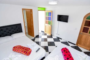A hotel room with a checkered floor, a bed with a black headboard, a TV mounted on the wall, and a wooden door with a green frame.