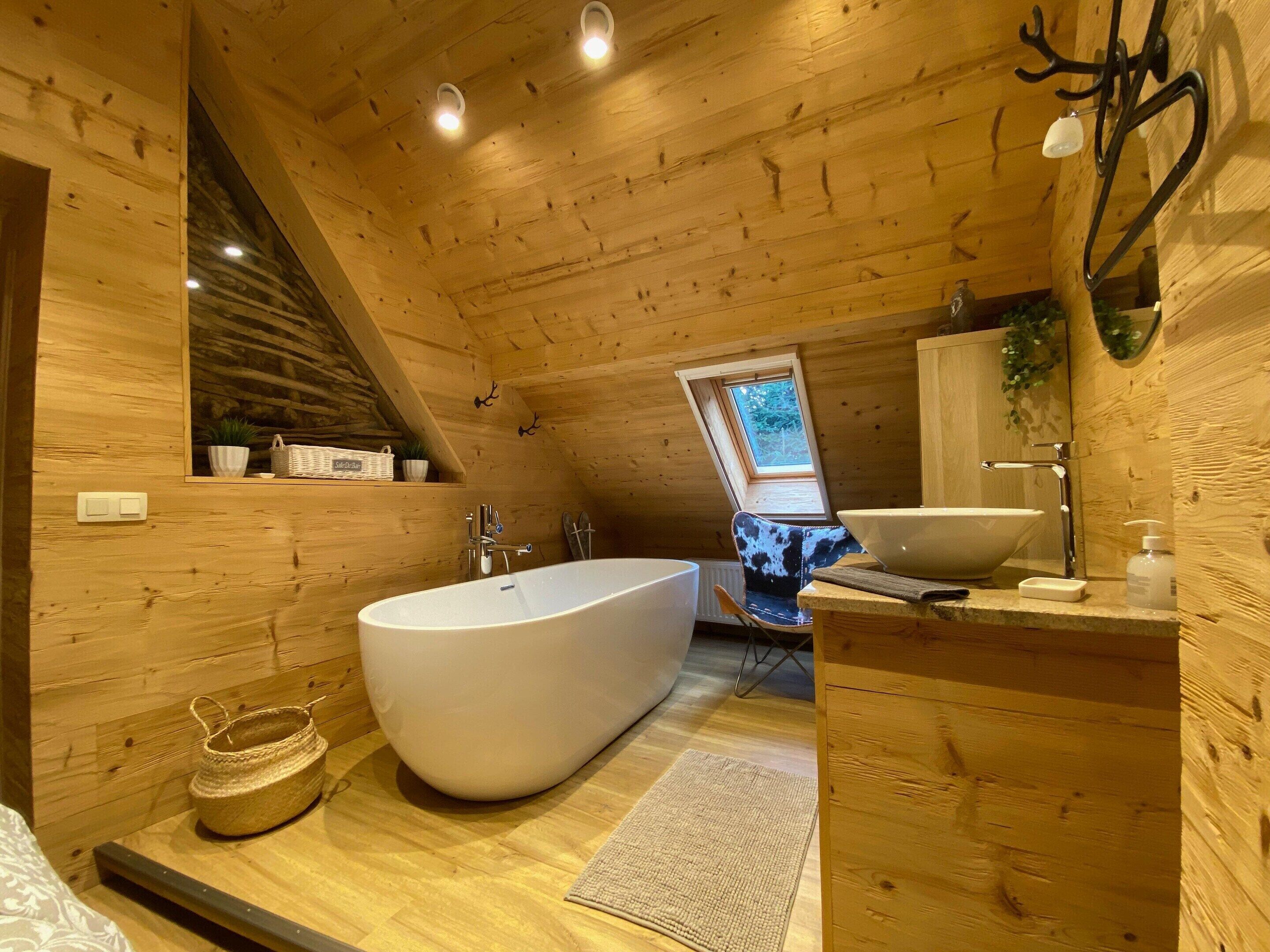 Een houten badkamer met een vrijstaand bad, een wastafel en een raam.