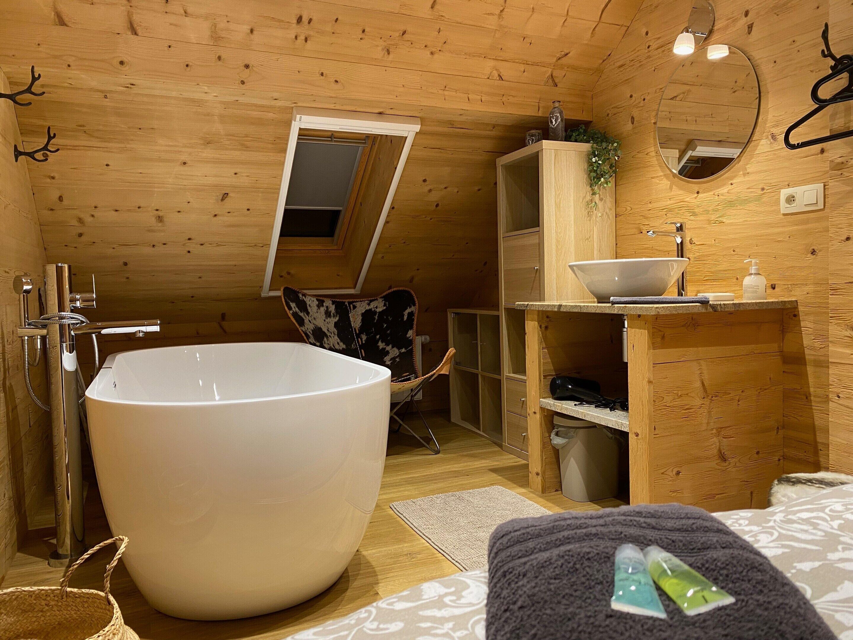 A wooden cabin bathroom with a large bathtub, a mirror, a sink, and a chair.