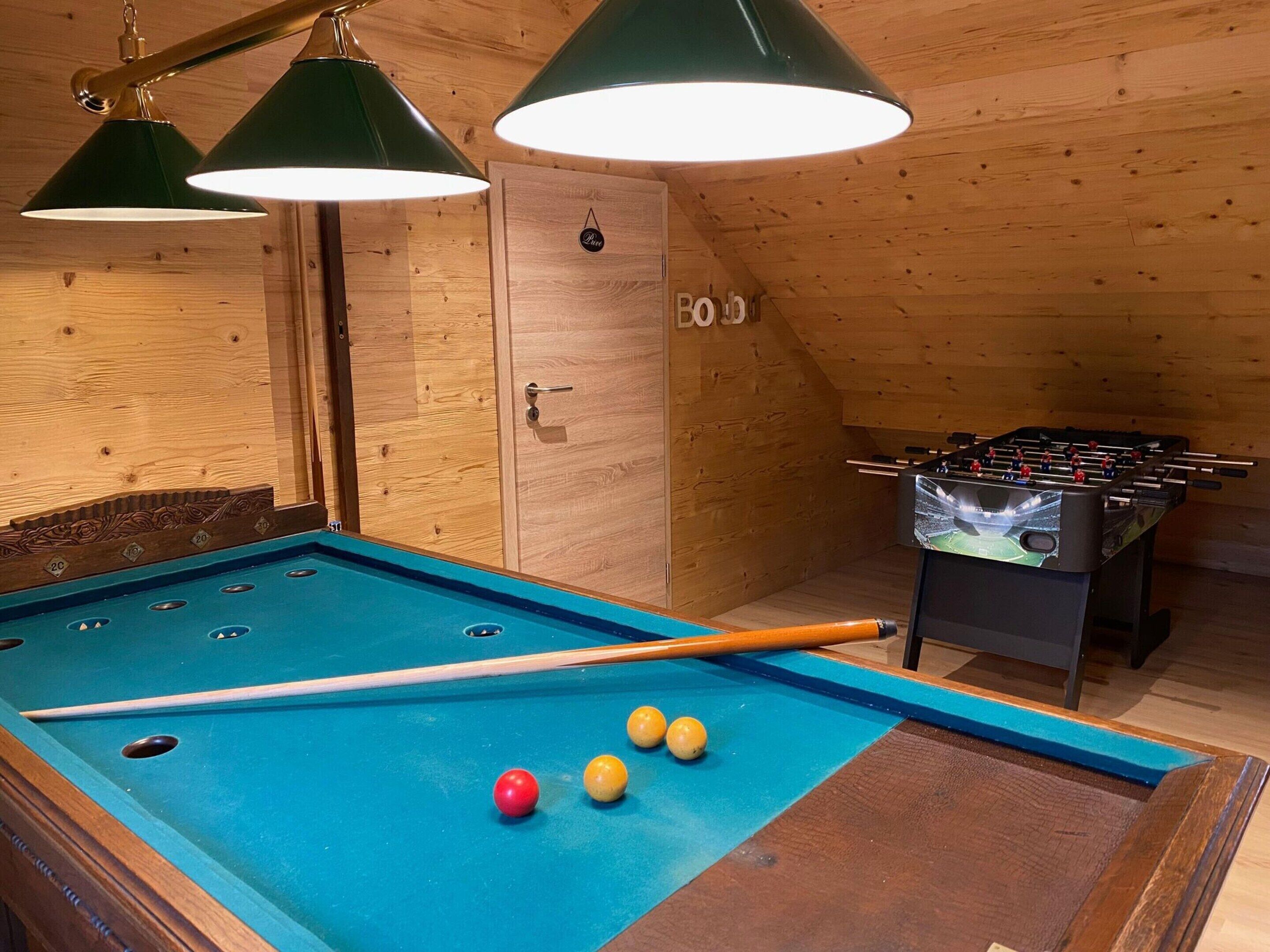A pool table with balls, a foosball table, and wooden walls.