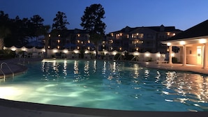 Una piscina al atardecer con una valla de piquetes blancos y edificios iluminados al fondo.