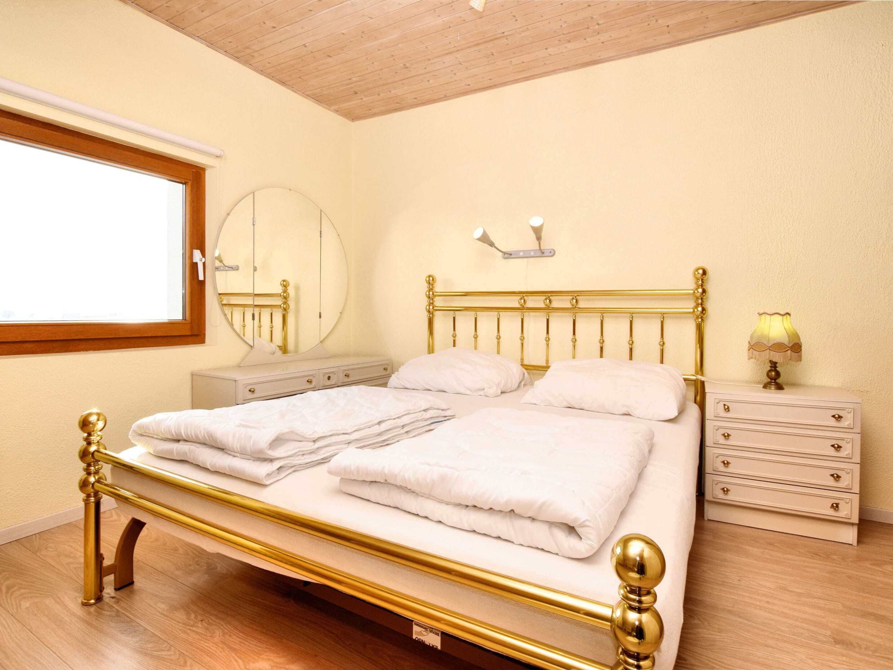 A bedroom with a double bed, a bedside table, a lamp, a mirror, and a window.