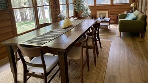 A wooden cabin interior with a dining table, chairs, a sofa, and large windows. - Cedarwood Lake House (Toccoa)