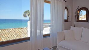 A bedroom with a large window overlooking a beach and a palm tree.