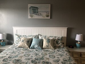 A bedroom with a bed, two bedside tables, a nightstand, a wall-mounted painting, and a window.