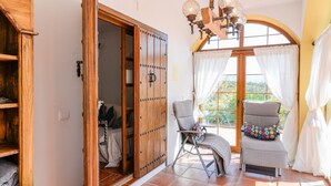 Ein Zimmer mit Holzschrank, Stuhl, Sofa und einem großen Fenster mit Vorhängen.