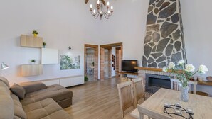 A modern living room with a sofa, a dining table with chairs, a fireplace, and a TV. - Villa Dajabe Sayalonga by Ruralidays (Málaga)
