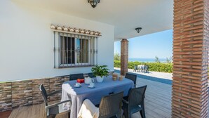 A covered outdoor dining area with a table set for two, a potted plant, and a view of the sea. - Villa Dajabe Sayalonga by Ruralidays (Málaga)