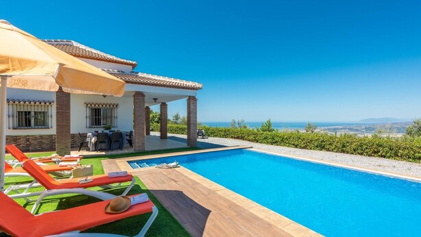 A poolside area with lounge chairs, a dining table, and a view of the sea. - Villa Dajabe Sayalonga by Ruralidays (Málaga)