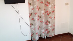 Une pièce dotée d’un téléviseur à écran plat fixé au mur, d’un rideau à motifs floraux et d’un sol carrelé.