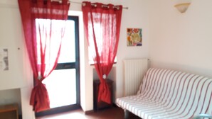 Une pièce avec un canapé, un radiateur et une porte ornée de rideaux rouges.