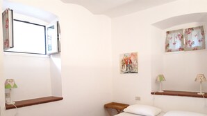 Une chambre avec deux lits, une fenêtre, un tableau et un petit tabouret en bois.