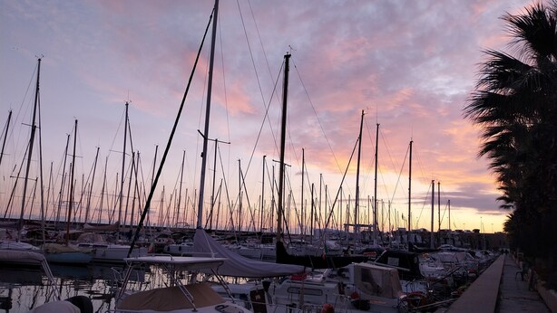 Un port de plaisance où de nombreux bateaux sont amarrés, une surface d’eau calme et un ciel au coucher du soleil.