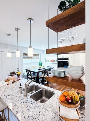 A modern kitchen with a granite countertop, stainless steel sink, and a wooden dining table with chairs. - Starlanding House: Downtown, Trails, Museums, Read the reviews- we'll spoil you! (Bentonville)