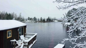 Une cabane en bois dotée d’une terrasse et d’un quai s’avançant dans un lac, le tout entouré d’arbres couverts de neige.
