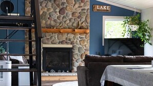 Un salon chaleureux avec une cheminée en pierre, un ventilateur de plafond, un mur en pierre et une enseigne sur laquelle on peut lire « LAC ».