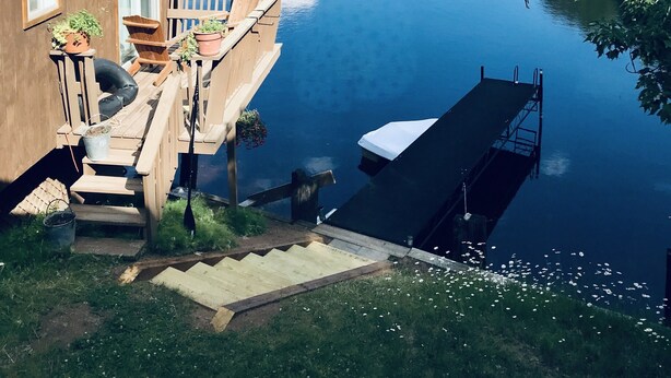 Une maison avec un quai s’avançant dans un lac paisible, entourée d’arbres et sous un ciel dégagé.