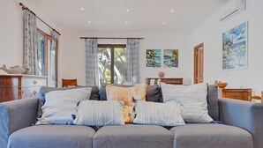 A living room with a grey sofa, patterned cushions, and artwork on the walls. - Ca Na Marieta House next to the beach with sea views and large garden (Portocolom)
