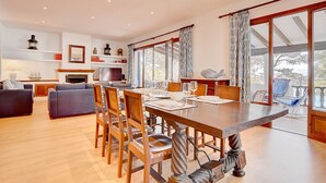 A spacious dining area with a long wooden table and chairs, a fireplace, and large windows with curtains. - Ca Na Marieta House next to the beach with sea views and large garden (Portocolom)
