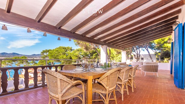 A covered outdoor dining area with wicker chairs and a wooden table, overlooking a scenic landscape. - Ca Na Marieta House next to the beach with sea views and large garden (Portocolom)