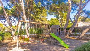 A playground with a swing set, slide, and wooden climbing structure. - Ca Na Marieta House next to the beach with sea views and large garden (Portocolom)