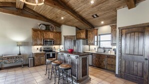 Une cuisine rustique avec des meubles en bois, un îlot central doté de tabourets et une grande porte.