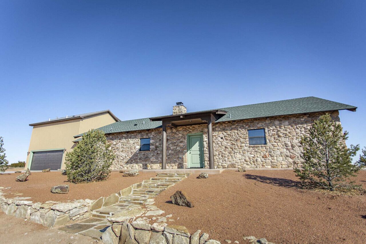 Una casa in pietra su due piani con una porta verde, un garage e una scala in pietra che conduce all'ingresso.