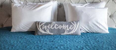 Una cama con cabecera capitonada, una colcha azul con textura y tres almohadas blancas.