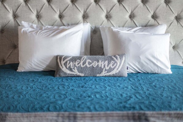 Una cama con cabecera capitonada, una colcha azul con textura y tres almohadas blancas.