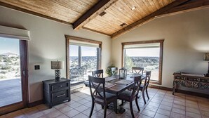 Une salle à manger spacieuse avec un plafond en bois, de grandes fenêtres offrant une vue sur le paysage et une table à manger entourée de chaises.